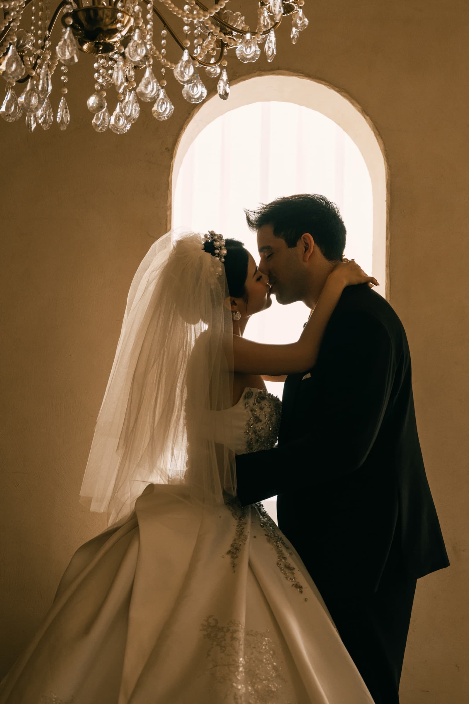 The couple sharing a kiss beneath a chandelier